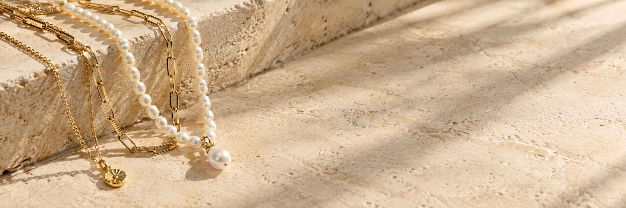 Gold and pearl jewelry on sunlit ivory stone